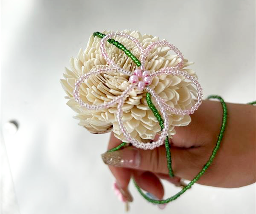 A woman holds a home-made flower that includes beads and plastic petals.