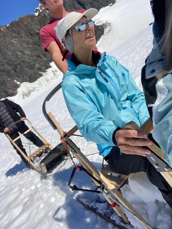 A woman wearing a jacket and hat sits on a dog sled in Alaska.