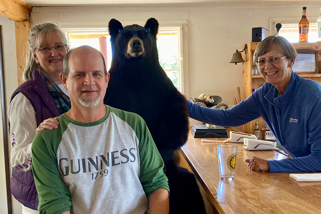 Two women and a man pose for a photo with a taxidermy bear at a store.
