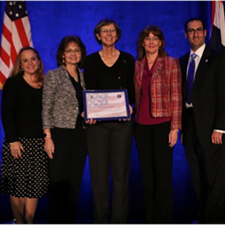 Four women and one man hold a certificate and smile during an awards recognition.