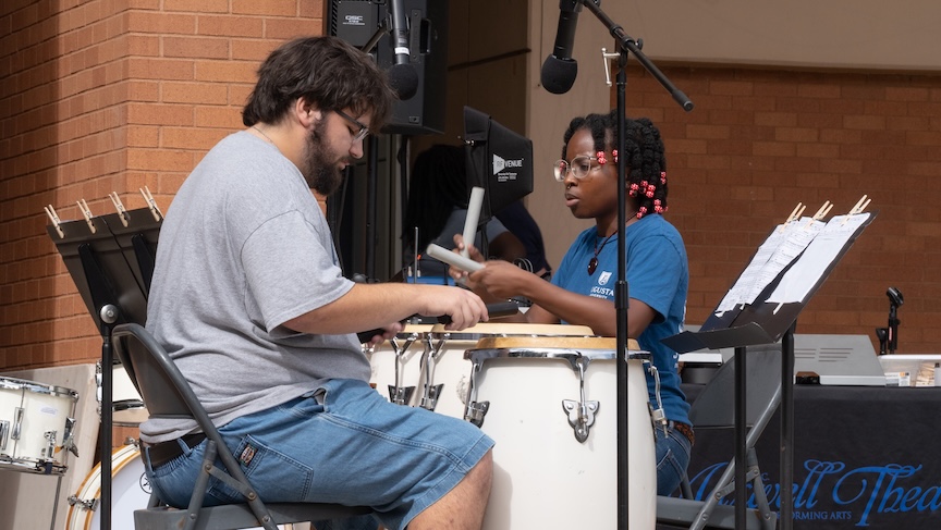 Two college students play the drums during an outdoor concert.