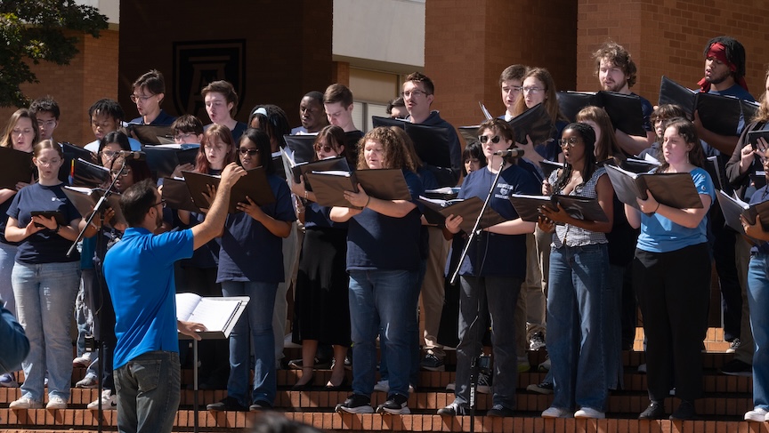 A large college choir sings during an outdoor performance.