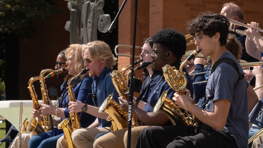 College students playing musical instruments during an outdoor performance.