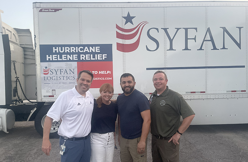 Three men and a woman stand in front of a tractor trailer with the name "Syfan" on it.