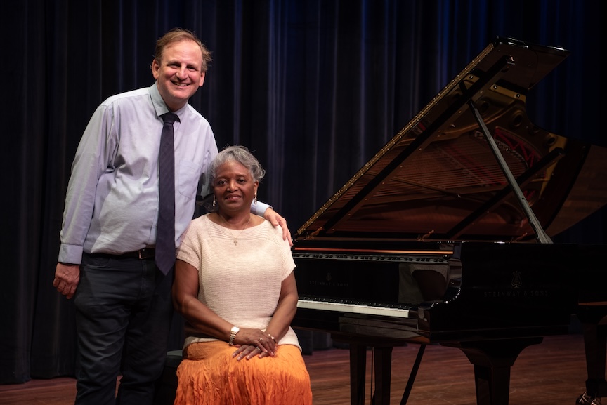 One male and one female smiling with a piano