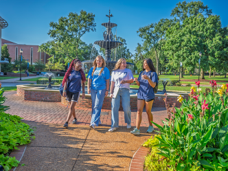 Four college women walk along a brick path on a college campus.