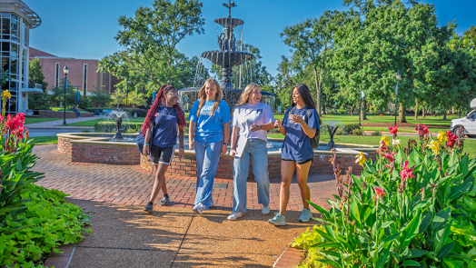 Four college women walk along a brick path on a college campus.