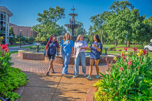 Four college women walk along a brick path on a college campus.