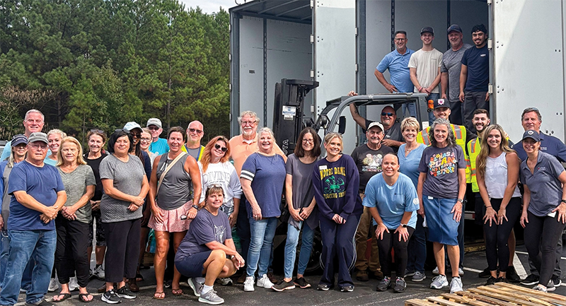A large group of people father around the back of a tractor trailer to celebrate sending supplies to people in need after a natural disaster.