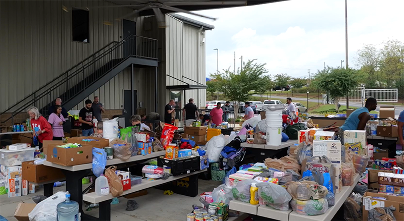 A large group of people help set up tables with necessities following a natural disaster.
