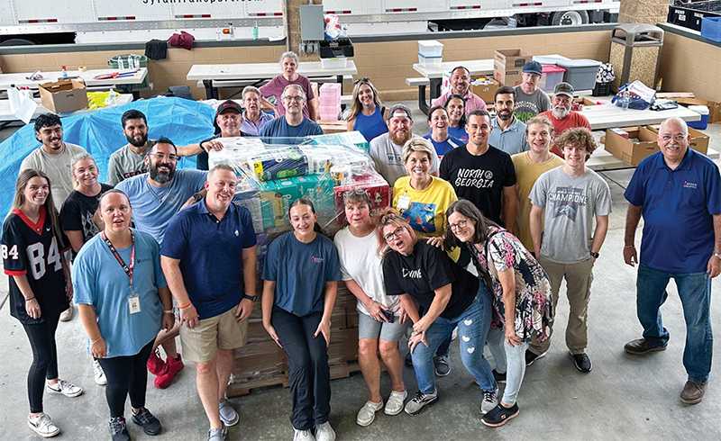 Large group of employee stand in front of bulk supply stacks