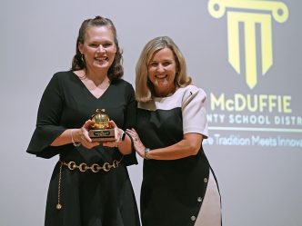 Two women smiling while one holds a trophy