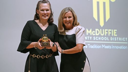 Two women smiling while one holds a trophy