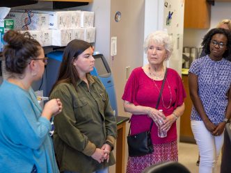 An older woman is given a tour of a scientific lab by three female college students.