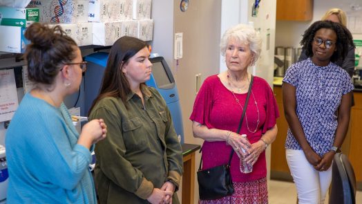 An older woman is given a tour of a scientific lab by three female college students.
