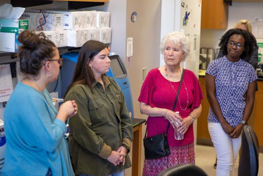 An older woman is given a tour of a scientific lab by three female college students.
