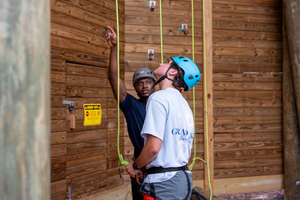 While on belay, two men stand near a climbing wall.