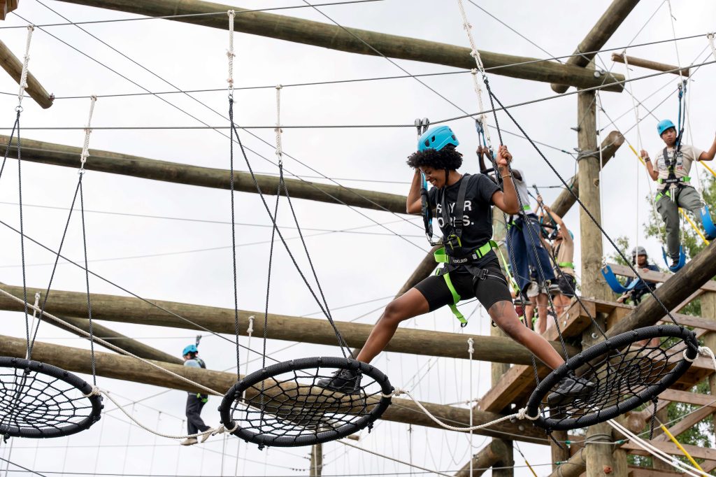 A female college student, in the air, on a challenge course.