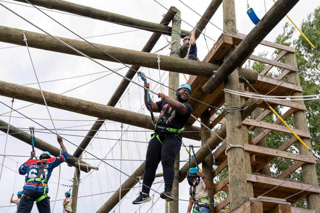 A male college student, in the air, on a challenge course.