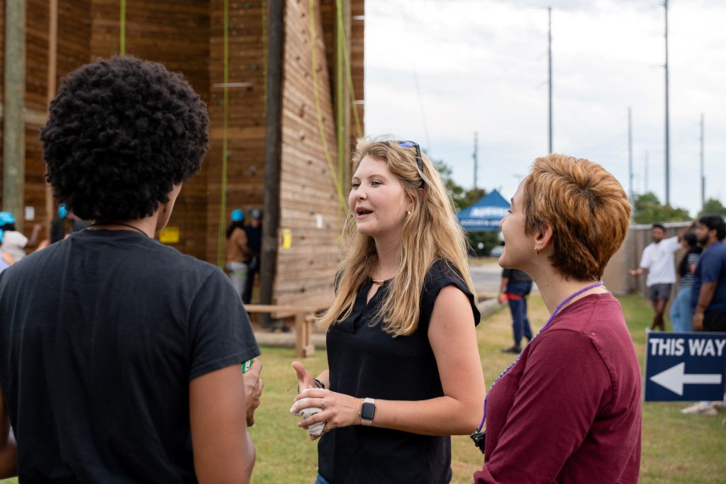 A college-aged girl stands in the center of the photo laughing around others.