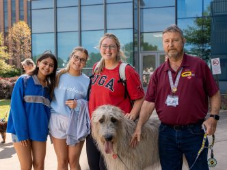Three college-aged female students pose for a photo with a man and a therapy dog.
