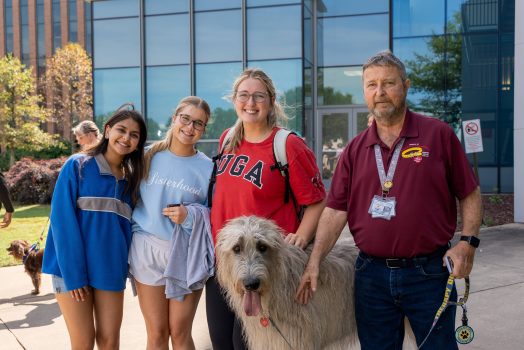 Three college-aged female students pose for a photo with a man and a therapy dog.