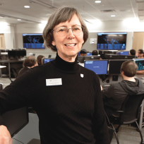A female computer sciences professor sits in a chair in a classroom and smiles at the camera.