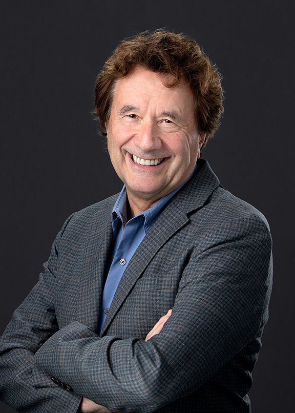 A man in a suit coat stands with his arms crossed.