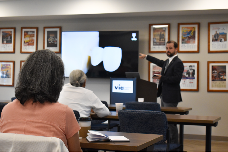 A man stands at the front of a classroom and presents to a group of people. He is pointing to a screen that shows x-rays.