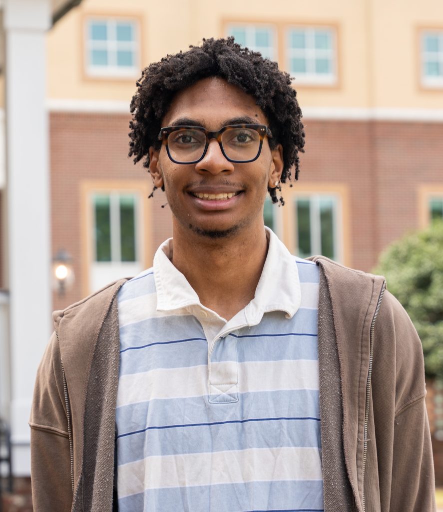 A college-aged male student poses for a photo outdoors.