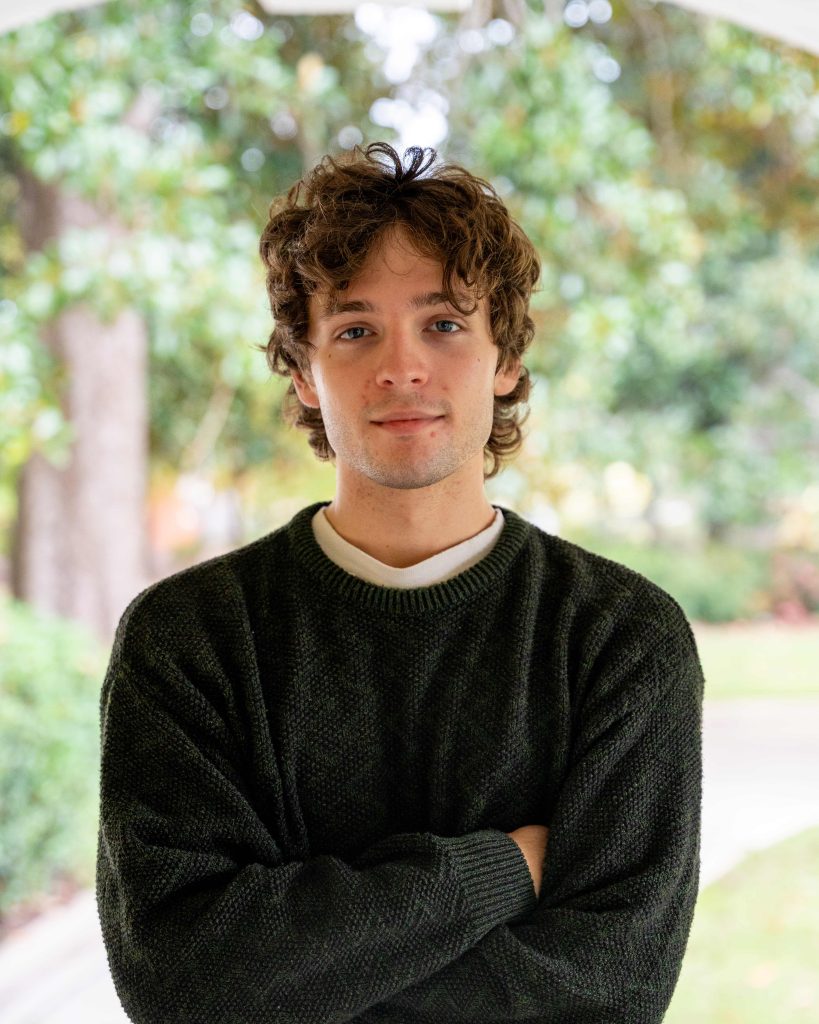 A college-aged male student poses for a photo outdoors.
