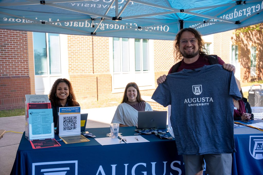 A man holds up a T-shirt in front a table.
