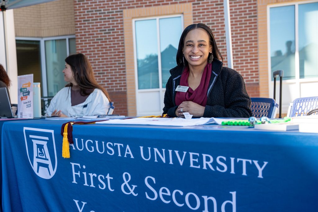 A woman smiling for a photo while sitting at a table outside of a college building.