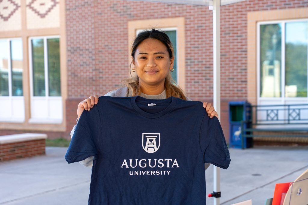 A college-aged girl holds up a T-shirt.
