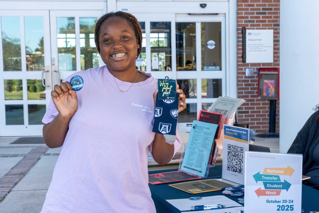 A college-aged woman smiles for a photo while holding a button and a pair of socks.