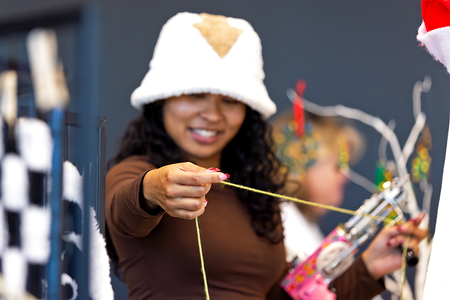 A college-aged woman smiles as she loads her rug tufting gun to begin working on a rug.