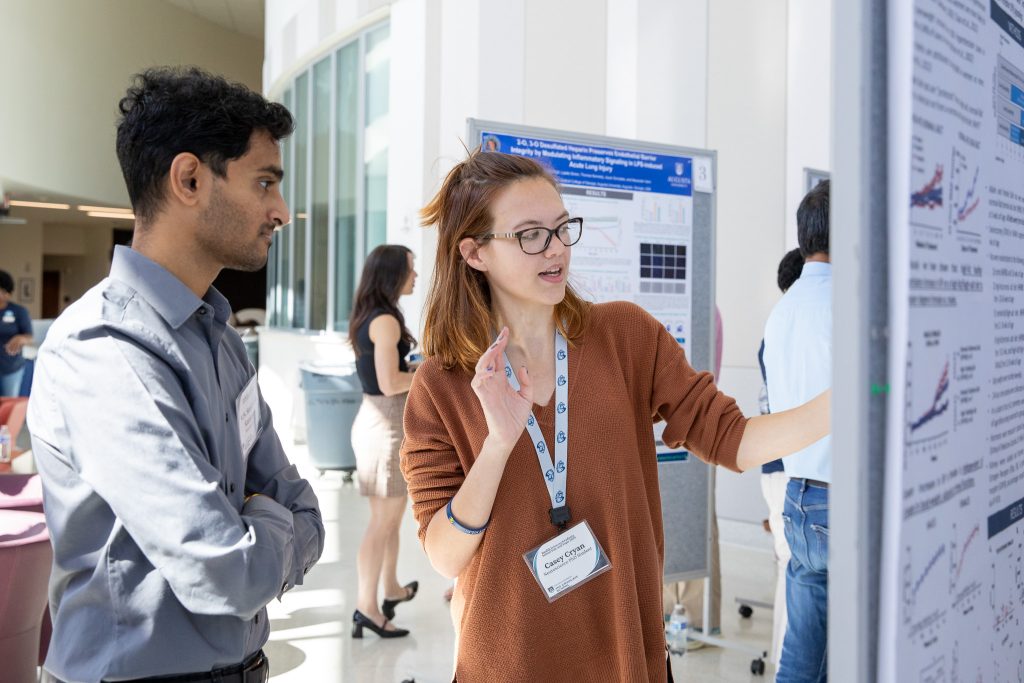 A female graduate student talks about her scientific research poster with an undergraduate student looking to continue his education.