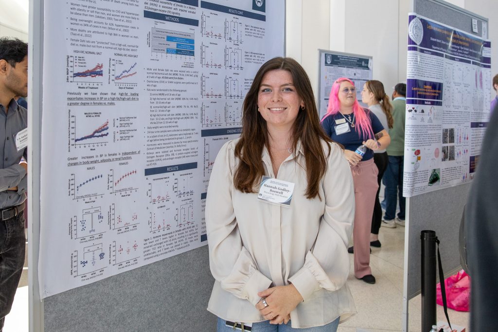 A female college student stands next to a scientific research poster during a big event.