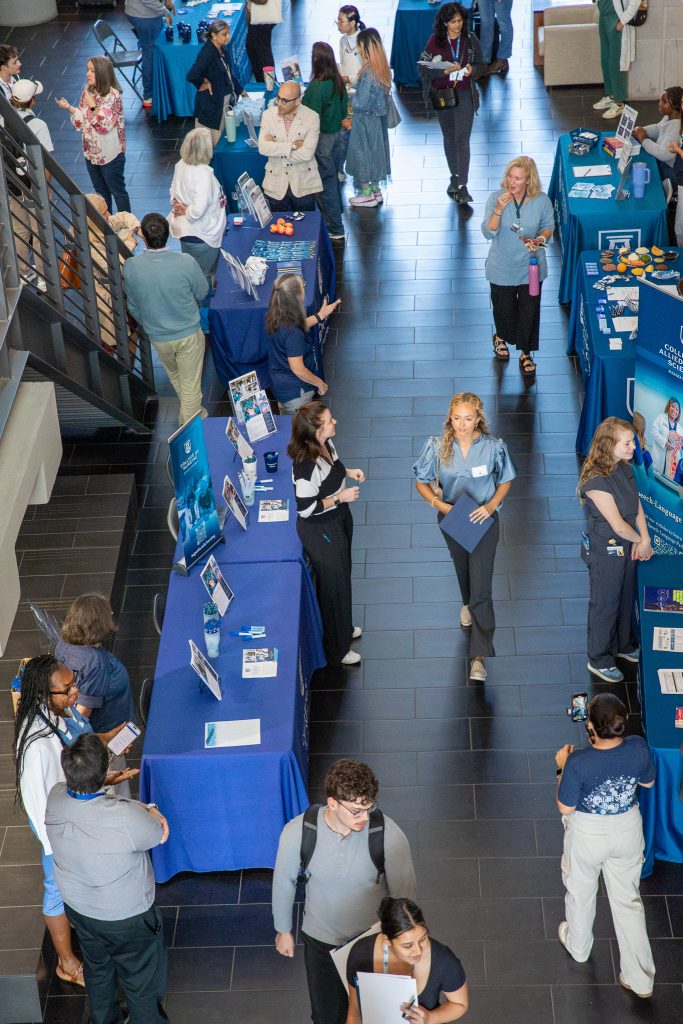 College students speak with recruiters and faculty for graduate programs during an expo and information session on a college campus.
