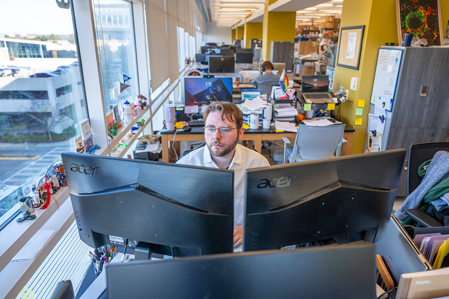 A male college student works at a computer in a scientific lab.