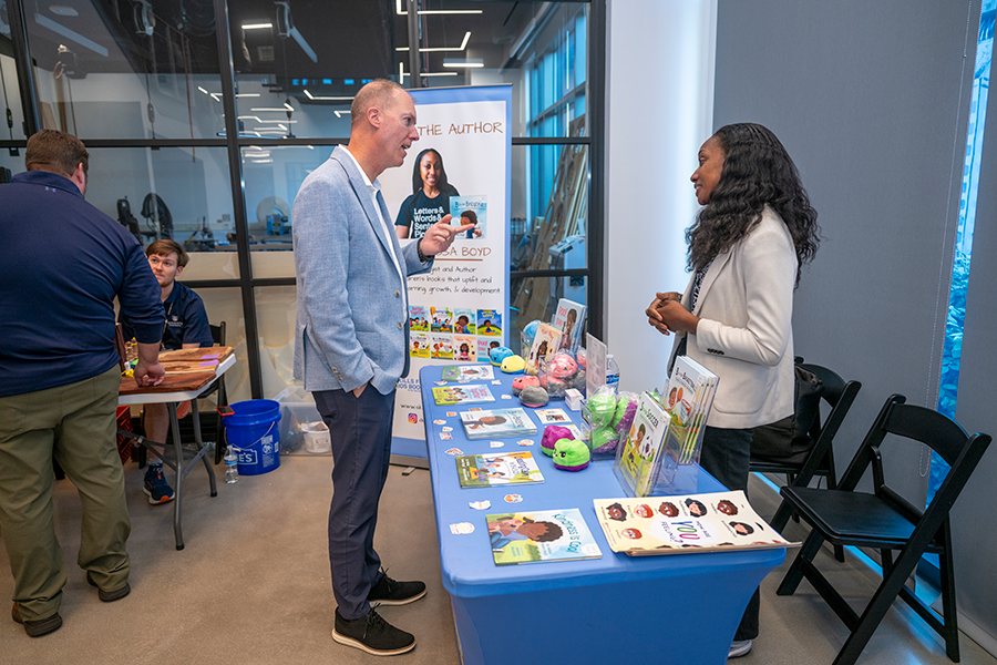A man speaks to a woman who is standing at a booth at a small business market.
