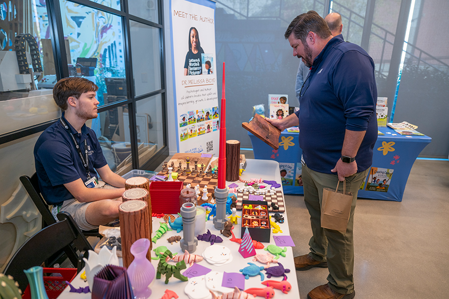 A man holds a piece of art and speaks to the artisan, a college-aged man, during a small-business market.