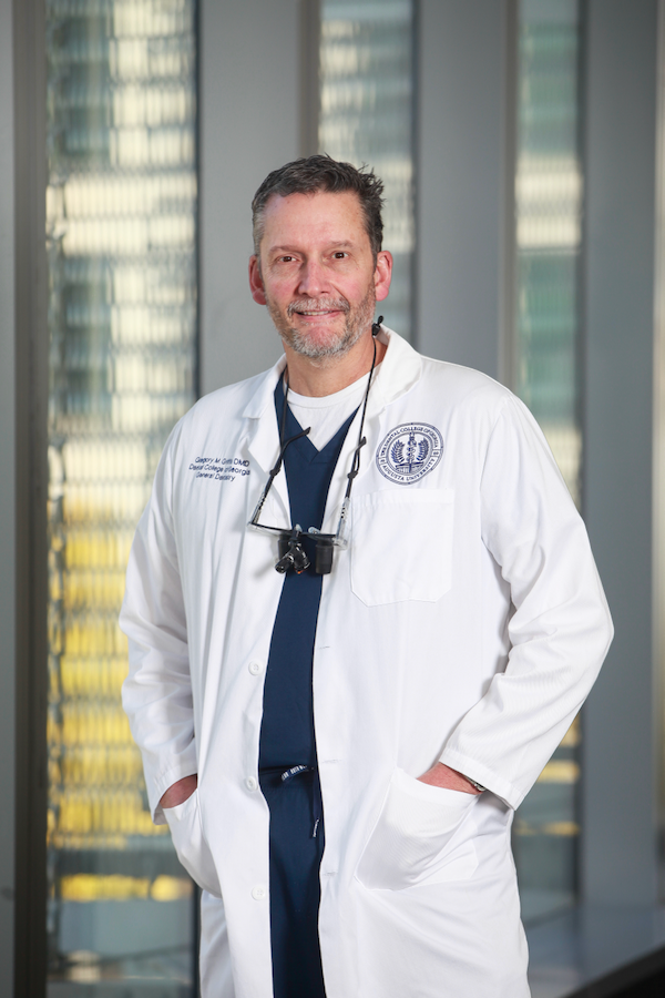 A male doctor in his lab coat stands in the hallway of a hospital.