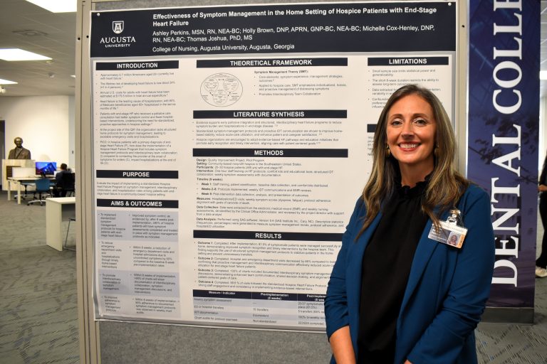 Woman in a blazer smiles in front of a poster project, she is in a library