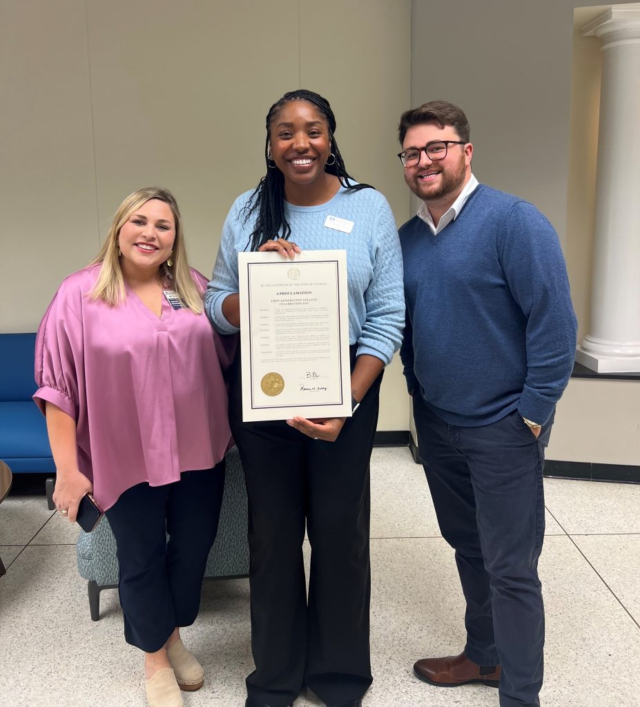 Two women and a man smile for a photo, with one woman holding up a proclamation.
