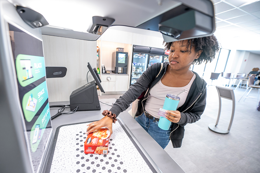 A college-aged woman uses a self-scanning machine to pay for food inside a market on a college campus.