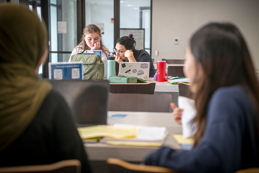 Four female college students sit at tables in a market inside a college library while studying.