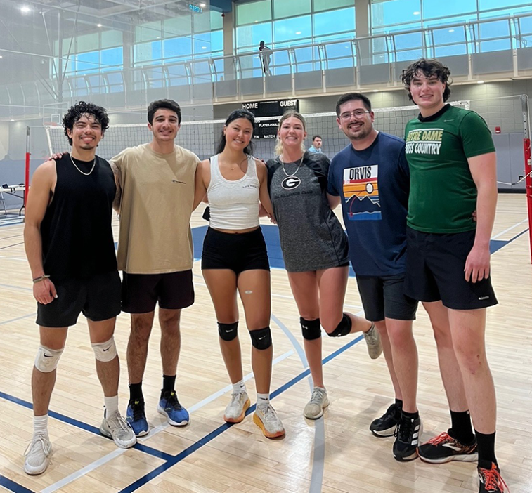 Two college-aged women and four college-aged men get ready to play a volleyball match.