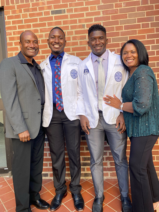 Two brothers wearing medical school lab coats pose for a photo with their parents.