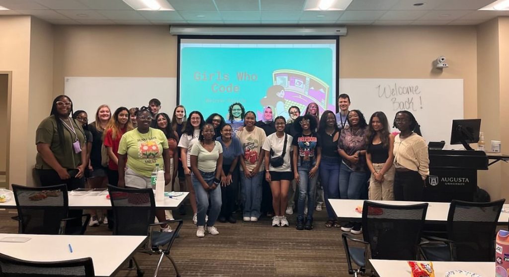 A large group of men and women pose for a photo at the front of a classroom